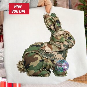 May include: A decorative bunny rabbit made from camouflage fabric. The bunny is in a seated position with its ears perked up. The fabric has shades of green, brown, and tan. The image also includes the text "PNG 300 DPI".