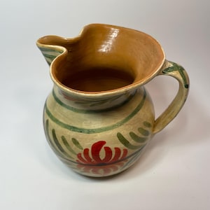 May include: A ceramic pitcher with a green and red floral design. The pitcher has a wide mouth and a handle.