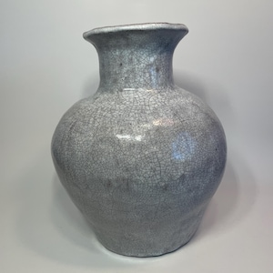 May include: A gray ceramic vase with a crackle glaze finish. The vase has a rounded body and a flared neck. The surface is covered in a network of fine cracks, giving it a textured appearance. The vase is a decorative item.