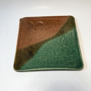 May include: A square ceramic plate featuring a two-tone glaze design. One section is a textured, earthy brown, while the other is a vibrant, glossy green. The two colors are separated by a diagonal line, creating a distinct contrast across the surface.