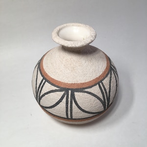 May include: A small, round, off-white ceramic vase with a textured surface. The vase features a decorative band of black and brown geometric designs around the middle. The opening is white and slightly flared.