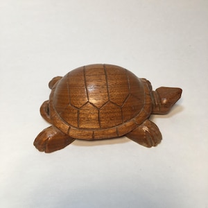May include: A detailed, wooden turtle figurine. The turtle is carved from a rich, brown wood, with visible grain patterns. The shell is segmented, and the head and limbs are well-defined. A decorative item.