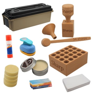 May include: A set of crafting supplies including a wooden stamp, a wooden spoon, a wooden funnel, a wooden box with 24 holes, a blue and yellow paper punch, a tin of balm, a stack of three round bars of wax, a glue stick, a pack of 54 wooden sticks, and a stack of white paper.