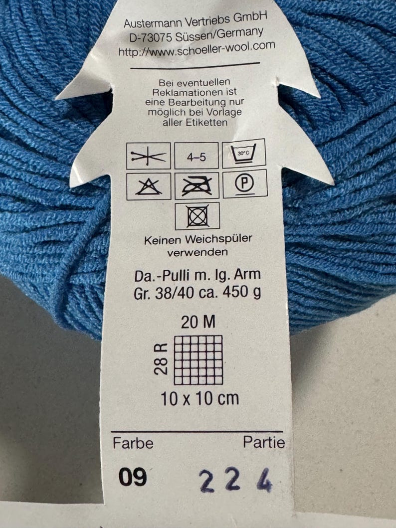 Puede incluir: Una madeja de lana azul con una etiqueta blanca. La etiqueta incluye instrucciones de lavado, un patr&oacute;n de punto y el texto "Da.-Pulli m. Ig. Arm Gr. 38/40 ca. 450 g 20 M 28 R 10 x 10 cm Farbe 09 Partie 224".