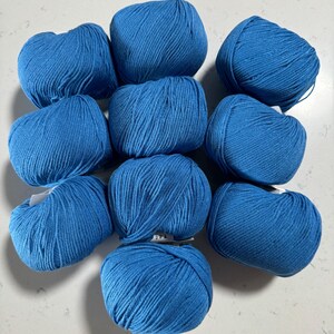 Puede incluir: Diez ovillos de lana azul dispuestos en c&iacute;rculo sobre una superficie blanca.