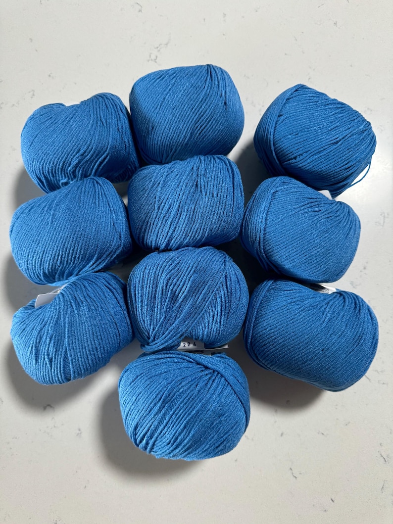 Puede incluir: Diez ovillos de lana azul dispuestos en c&iacute;rculo sobre una superficie blanca.