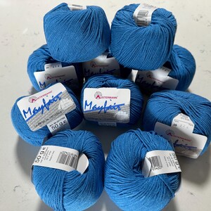 Puede incluir: Una colecci&oacute;n de diez ovillos de lana azul con etiquetas blancas que dicen "Mayfair" y "Austermann". Cada ovillo pesa 50 gramos.