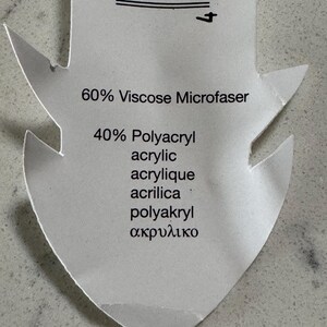 Puede incluir: Una etiqueta de tela blanca con texto negro que indica la composici&oacute;n de la tela: 60% Viscosa Microfaser, 40% Poliacr&iacute;lico Acr&iacute;lico Acr&iacute;lico Acrilica Poliakryl &alpha;&kappa;&rho;&upsilon;&lambda;&iota;&kappa;ό