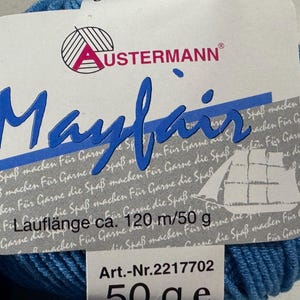 Puede incluir: Una madeja de lana azul con la etiqueta "Mayfair" y la marca "USTERMANN". El texto "Laufl&auml;nge ca. 120 m/50 g" y "Art.-Nr. 2217702 50 ge" tambi&eacute;n es visible.