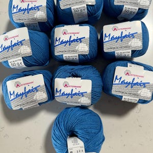 Puede incluir: Diez ovillos de hilo azul etiquetados como "Mayfair" por Austermann. Cada ovillo pesa 50 gramos y tiene una longitud de 120 metros. El hilo es de peso medio y es adecuado para tejer o hacer ganchillo.