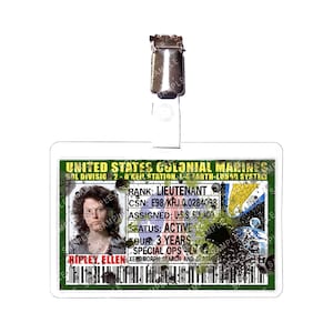 Può includere: Un badge identificativo rettangolare con una clip di plastica trasparente. Il badge presenta il testo "UNITED STATES COLONIAL MARINES" e una foto di una donna. Il testo aggiuntivo include "RANK: LIEUTENANT" e "RIPLEY, ELLEN."
