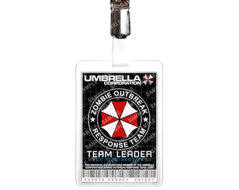 May include: A white plastic ID card with a black and red logo for the Umbrella Corporation Zombie Outbreak Response Team. The logo features a red umbrella with a white background and a black star on each side. The text "Team Leader" is printed in black on the card. The card number 8957-755-8689 is printed in black on the card.