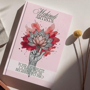 May include: A pink book titled "Mehndi Artists" with a lotus flower illustration and the text "Your Complete Course From Beginner To Pro." The cover features a hand holding the flower, with red watercolor-style accents.