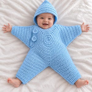 May include: A light blue crocheted star-shaped bunting with a hood and two matching circular buttons on the chest. The garment features a textured stitch pattern and is designed with long sleeves and legs, forming a five-pointed star silhouette.