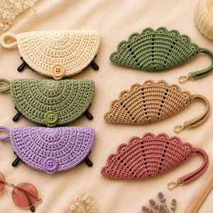 May include: Six semi-circular crochet cases for eyewear, three featuring button closures and three with scalloped edges and wrist straps. The cases are in cream, sage green, lavender, olive green, tan, and dusty rose colors.