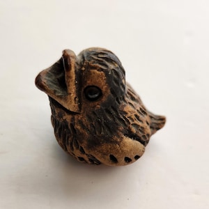May include: A small, handcrafted ceramic bird figurine in shades of brown. The bird has a detailed, textured surface and a wide-open beak. The figurine is a unique decorative item, perfect for adding a touch of nature-inspired art to any space.