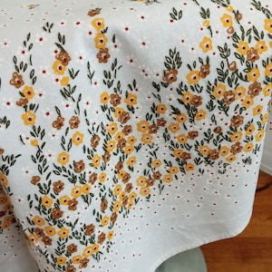 May include: White tablecloth with a floral pattern featuring small yellow and brown flowers with green leaves. The tablecloth has a white background with small red dots.