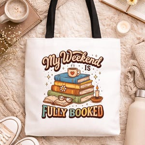 May include: White tote bag with black handles featuring the text "My Weekend is Fully Booked" in a retro font. The graphic includes a stack of books, a coffee cup, a candle, and glasses. Beige sneakers and a water bottle are also visible.