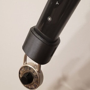 May include: A black Tesla key fob with a silver combination lock attached. The key fob has a small white circle on the side and the word "TESLA" printed on it.