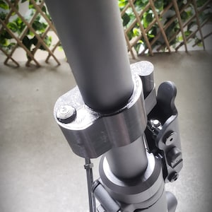 May include: Close-up of a black electric scooter handlebar with a folding mechanism and a black button. The handlebar is made of metal and has a textured finish.
