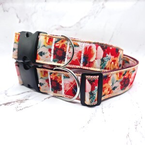 May include: Two floral dog collars. The collars display a vibrant pattern of red, orange, and yellow flowers on a beige background. Each collar has a black plastic buckle and a silver metal D-ring for leash attachment. The collars are stacked on top of each other.