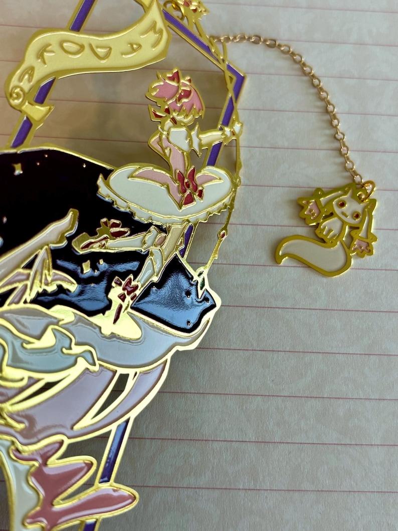 K&ouml;nnte beinhalten: Goldener Metall-Lesezeichen mit einer Comicfigur mit rosa Haaren und einem wei&szlig;en Kleid, die einen Zauberstab h&auml;lt. Die Figur ist von Sternen und einem Banner umgeben, auf dem "Today is my" steht, und eine kleine wei&szlig;e Katze mit rosa Ohren ist an der Kette des Lesezeichens befestigt.