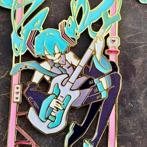 K&ouml;nnte beinhalten: Ein detaillierter Emaille-Pin mit einem Anime-Charakter mit t&uuml;rkisfarbenen Haaren, der eine wei&szlig;e und t&uuml;rkisfarbene Gitarre spielt. Der Pin hat goldfarbene Umrisse und rosa Akzente mit einem herzf&ouml;rmigen Detail. Der Charakter tr&auml;gt ein lila-t&uuml;rkisfarbenes Outfit.