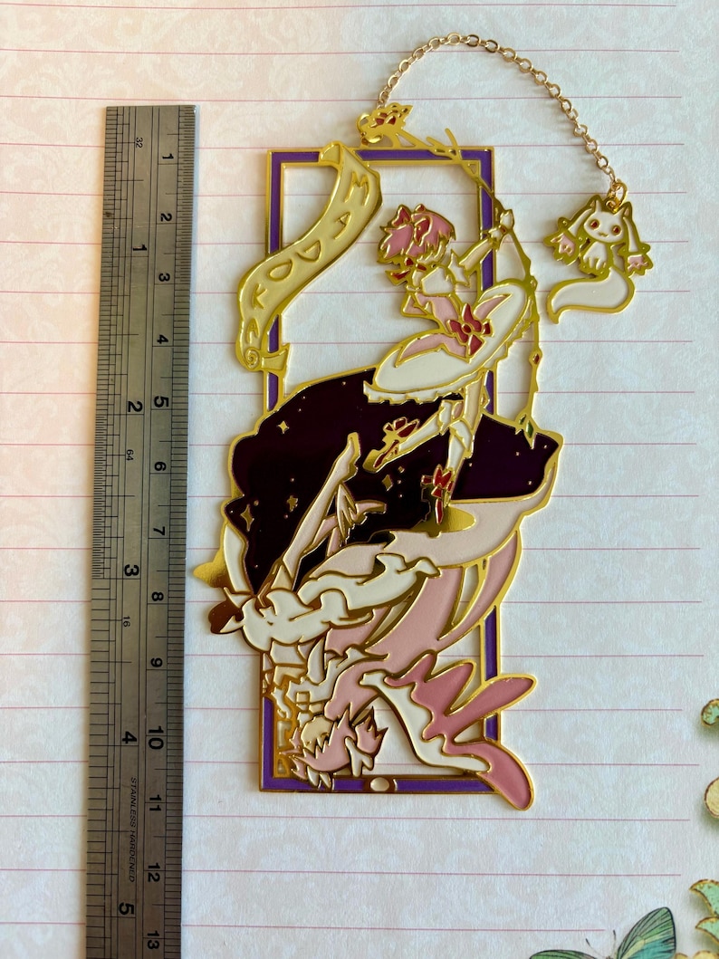K&ouml;nnte beinhalten: Goldener Metall-Lesezeichen mit einer Comicfigur mit rosa Haaren und einem wei&szlig;en Kleid, die eine Schriftrolle mit dem Wort "DO" h&auml;lt. Die Figur ist von Sternen und einem violetten Rahmen umgeben. Ein kleiner wei&szlig;er Hasenanh&auml;nger h&auml;ngt am Lesezeichen.