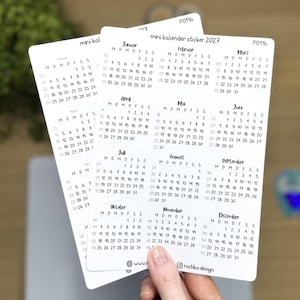 Könnte beinhalten: Ein weißer Aufkleberbogen mit einem Mini-Kalender für 2027 in schwarzer Schrift. Der Bogen zeigt die Monate Januar bis Dezember in einem Raster, wobei die Wochentage mit M, D, M, D, F, S, S beschriftet sind. Der Text lautet mini kalender sticker 2027.