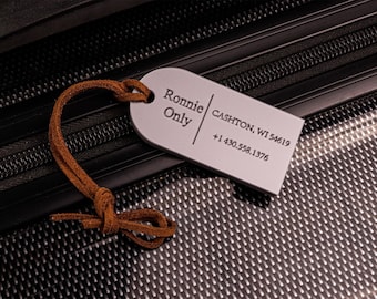 May include: White luggage tag with the text "Ronnie Only" and "CASHTON, WI 54619 +1 430.558.1376". The tag is attached to a brown leather strap.