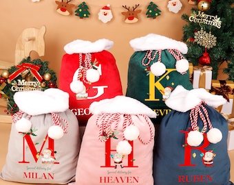 May include: Six Christmas gift bags in various colours, each with a white fluffy trim and drawstring closure. The bags display large letters, Santa Claus illustrations, and the words "Special delivery for" followed by a name.
