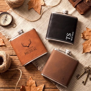 May include: Three stainless steel flasks with leather covers. One is black with "TS BEAT MAN" in white, another is brown with a deer antler design and "GROOMSMAN MICHEAL" in white, and the third is brown with a "K" in a diamond.