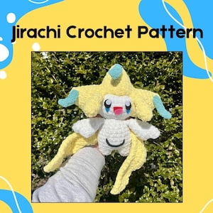 Puede incluir: Un juguete de peluche Jirachi Pokemon tejido a crochet con hilo amarillo y blanco. El juguete de peluche sostiene una cinta de deseos en sus manos. El juguete de peluche está sentado en un lecho de hojas verdes.