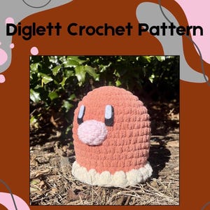 Może przedstawiać: Pluszowa zabawka Diglett wykonana na szydełku w kolorze różowym i białym. Zabawka siedzi na łóżku z brązowych liści i zielonej roślinności.