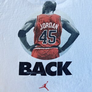 Pode incluir: Camiseta branca com uma imagem em preto e branco de um jogador de basquete vestindo uma camisa vermelha com o n&uacute;mero 45 e a palavra "JORDAN" nas costas. O texto "BACK" &eacute; impresso abaixo da imagem. Uma pequena silhueta de jogador de basquete vermelho e preto &eacute; impressa abaixo do texto.