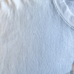 Pode incluir: Um close-up de uma camiseta cinza claro com uma textura lisa. O tecido parece ser de algod&atilde;o.