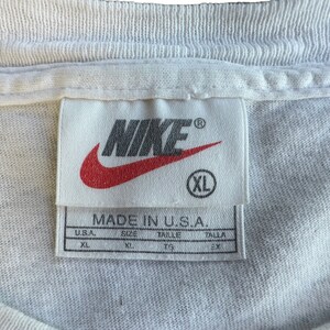 Pode incluir: Etiqueta de camiseta Nike branca com logo swoosh vermelho e o texto "MADE IN U.S.A.". A etiqueta tamb&eacute;m mostra o tamanho "XL" em tamanhos americano e internacional.
