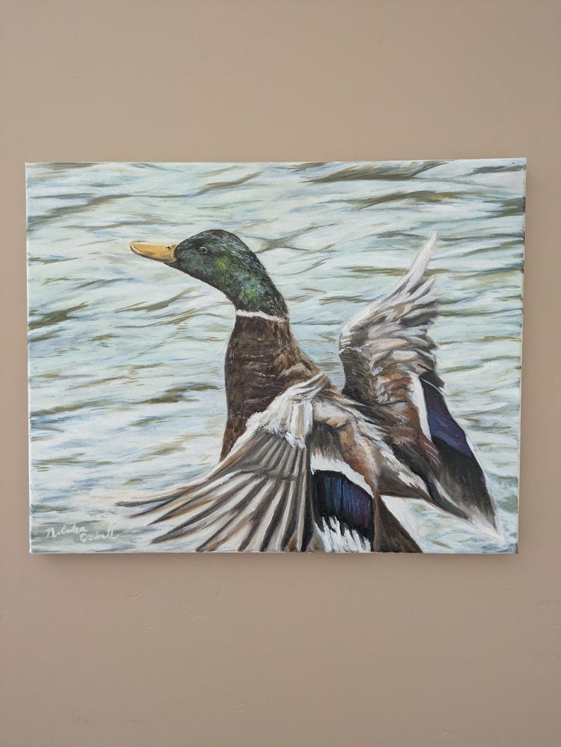 May include: Oil painting of a mallard duck with outstretched wings, set against a backdrop of water. The duck features a green head, brown body, and gray and blue wings. The artwork is signed in the lower left corner.