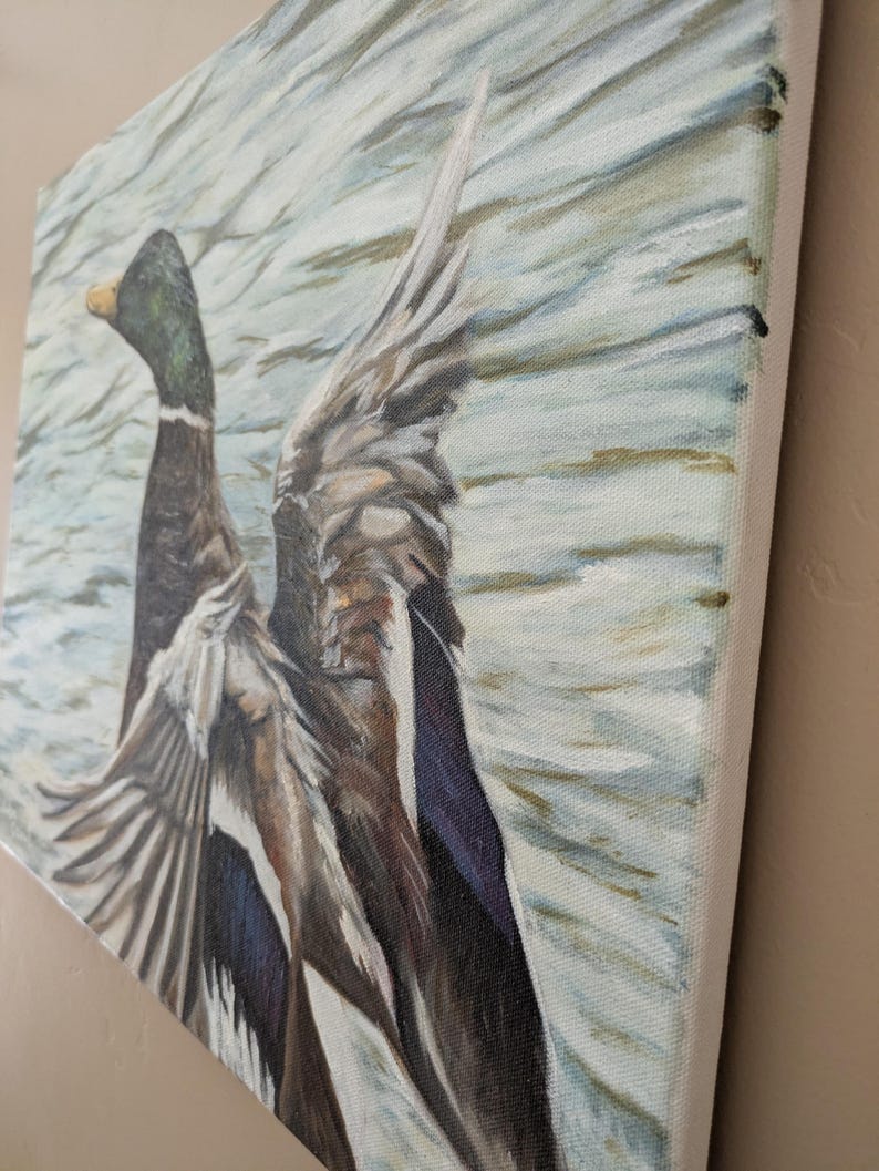 May include: A canvas painting depicts a duck with outstretched wings, set against a backdrop of water. The duck features a green head, brown body, and gray and blue wings. The artwork is rendered with visible brushstrokes, creating a textured effect.
