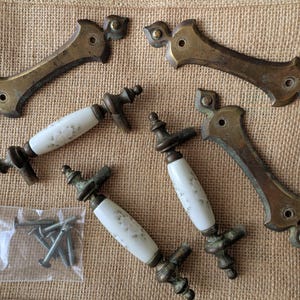 以下が含まれることがあります： 真鍮と磁器製のアンティークキャビネット金具のコレクション。真鍮製のハンドルと、花の模様が入った磁器製のプルが含まれています。ネジの小袋も付属しています。金具はヴィンテージで、古びた外観をしています。