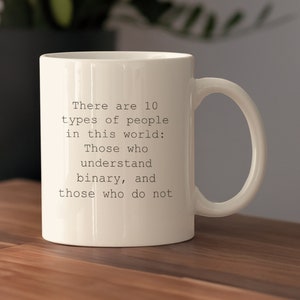 Puede incluir: Taza de cerámica blanca con una cita de texto negro: "Hay 10 tipos de personas en este mundo: Los que entienden binario, y los que no."