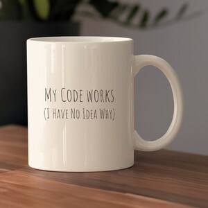 Może przedstawiać: Biały ceramiczny kubek do kawy z czarnym tekstem, który brzmi "Mój kod działa (nie mam pojęcia dlaczego)".