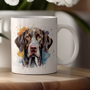 May include: White ceramic mug with a watercolor illustration of a brown and white dog with colorful paint splatters in the background.