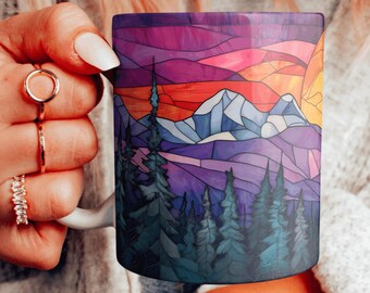 Könnte beinhalten: Eine weiße Keramiktasse mit einem bunten Glasmalereidesign eines Gebirges bei Sonnenuntergang. Das Design zeigt violette, blaue, rosa, orange und gelbe Farbtöne.