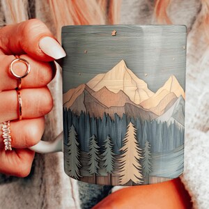 May include: A ceramic coffee mug with a wood-look design featuring a mountain range and forest scene. The mug has a light blue background with brown and green accents. The design is reminiscent of a wood carving.