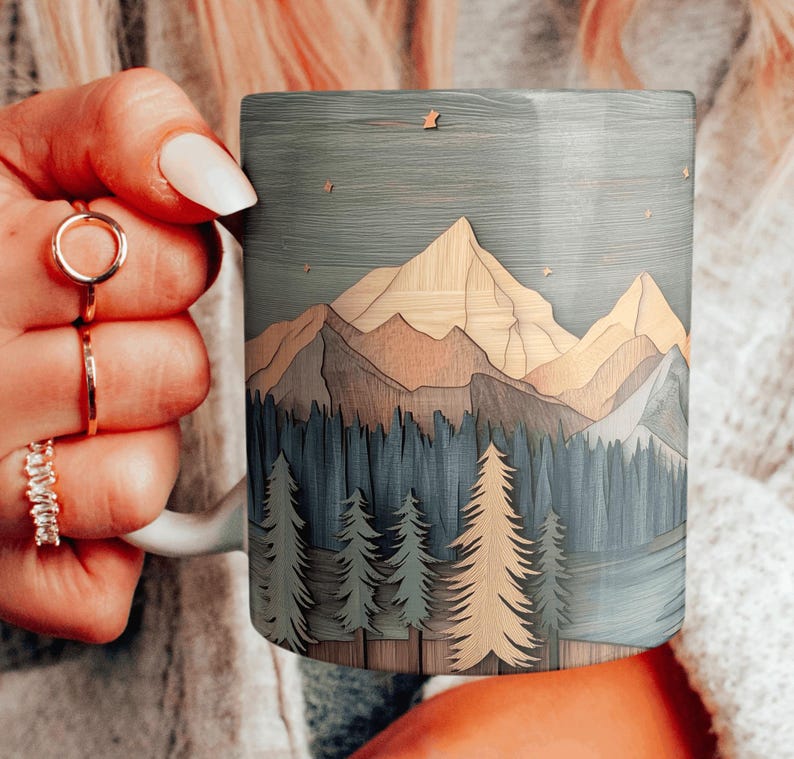 May include: A ceramic coffee mug with a wood-look design featuring a mountain range and forest scene. The mug has a light blue background with brown and green accents. The design is reminiscent of a wood carving.