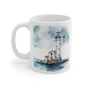 May include: White ceramic mug with a watercolor illustration of a lighthouse on a small island. The lighthouse is white with a red roof and a red light at the top. The sky is blue with white clouds. The water is blue and there are rocks around the island.