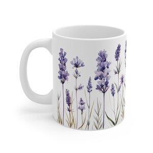 May include: White ceramic mug featuring a watercolor design of lavender sprigs in shades of purple and green. The floral pattern is arranged against a white background. The mug has a curved handle.