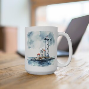 May include: White ceramic mug with a watercolor illustration of a lighthouse on a rocky island. The lighthouse is white with a red roof and a black and white striped tower. The sky is a light blue with gray clouds.