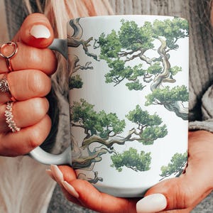 May include: White ceramic mug with a repeating pattern of green bonsai trees. The trees have brown branches and green leaves.